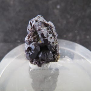 Może przedstawiać: Gromada ciemnofioletowych, metalicznych, kryształowych okazów minerałów. Kryształy są zebrane w szorstki, nieregularny kształt.