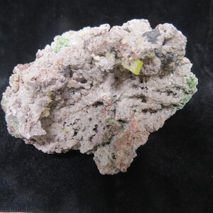 May include: A close-up of a rock with a white, grey, and brown surface. There are small, bright yellow and green crystals embedded in the rock.