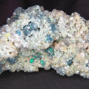 Peut inclure: Un amas de petits cristaux blancs, gris et verts. Les cristaux sont regroupés en une forme irrégulière et rugueuse.