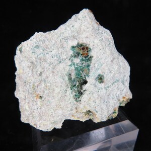 Può includere: Una roccia bianca ruvida con depositi minerali verdi e marroni. La roccia ha una superficie ruvida e irregolare e misura circa 12,5 cm di larghezza.