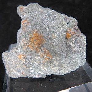 Può includere: Primo piano di una roccia grigia ruvida con macchie di cristalli marroni-arancioni. La roccia ha una superficie naturale irregolare e sembra essere un campione minerale.