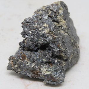 Könnte beinhalten: Ein rauer, grauer und silberner Stein mit einem Kristallhaufen. Der Stein hat eine raue, unebene Oberfläche und ist mit kleinen, glänzenden Kristallen bedeckt.