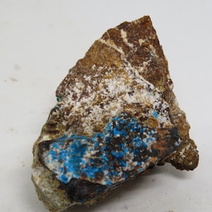May include: A rough, brown rock with white and blue mineral deposits. The blue mineral is clustered in a band across the bottom of the rock.
