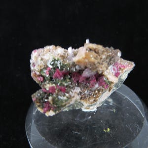 May include: A cluster of pink and green crystals on a brown matrix. The crystals are arranged in a random pattern and have a shiny, metallic luster.