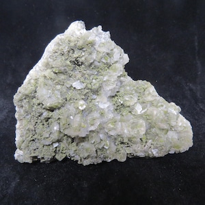May include: A cluster of clear, glassy crystals embedded in a matrix of green, moss-like material. The crystals have a rough, irregular texture and are arranged in a random pattern. The overall color of the specimen is a light green.