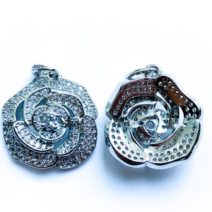 May include: Two silver rose-shaped pendants with clear crystal embellishments. The pendants are designed with a swirl pattern and have a shiny finish.