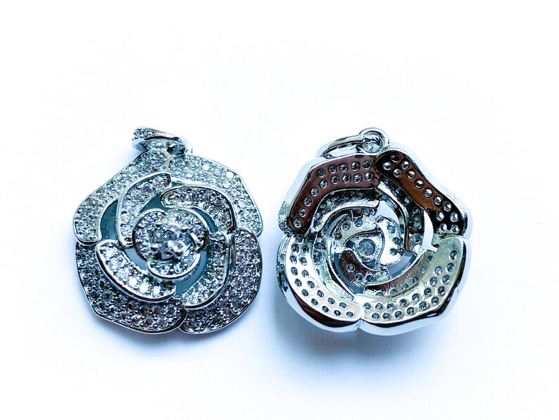 May include: Two silver rose-shaped pendants with clear crystal embellishments. The pendants are designed with a swirl pattern and have a shiny finish.