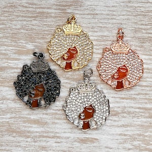 May include: Four black and brown metal charms featuring a woman with a crown and afro hair. The charms are decorated with rhinestones and come in gold, silver, rose gold, and black finishes.