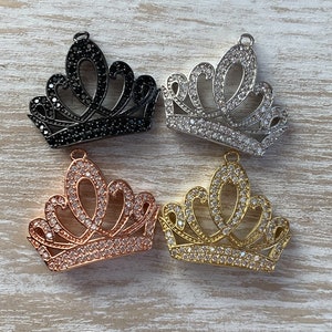 May include: Four crown charms in different finishes: black, silver, rose gold, and gold. Each charm is adorned with clear rhinestones.