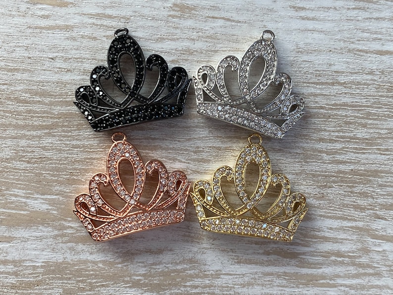May include: Four crown charms in different finishes: black, silver, rose gold, and gold. Each charm is adorned with clear rhinestones.