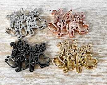Könnte beinhalten: Vier Anhänger in Silber, Roségold, Schwarz und Gold. Jeder Anhänger schreibt "Nurse Life" mit einem Stethoskop- und Herzdesign. Die silbernen und goldenen Anhänger haben klare Kristallakzente.