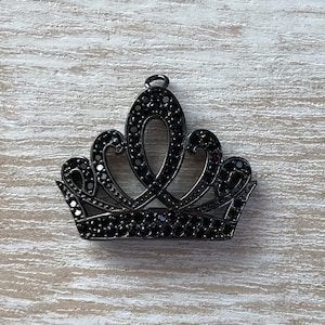 May include: A black metal crown charm with black rhinestone accents. The crown has a pointed top and a rounded base.