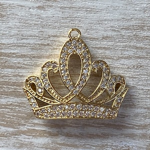 May include: Gold-tone crown charm with clear rhinestones. The crown has a pointed top and five points.