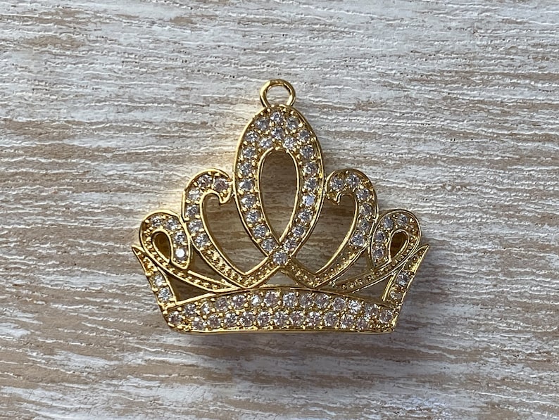 May include: Gold-tone crown charm with clear rhinestones. The crown has a pointed top and five points.