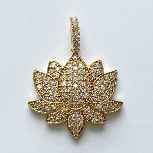 K&ouml;nnte beinhalten: Ein goldfarbener Anh&auml;nger mit einem Lotusblumen-Design, besetzt mit klaren Zirkonia-Steinen.