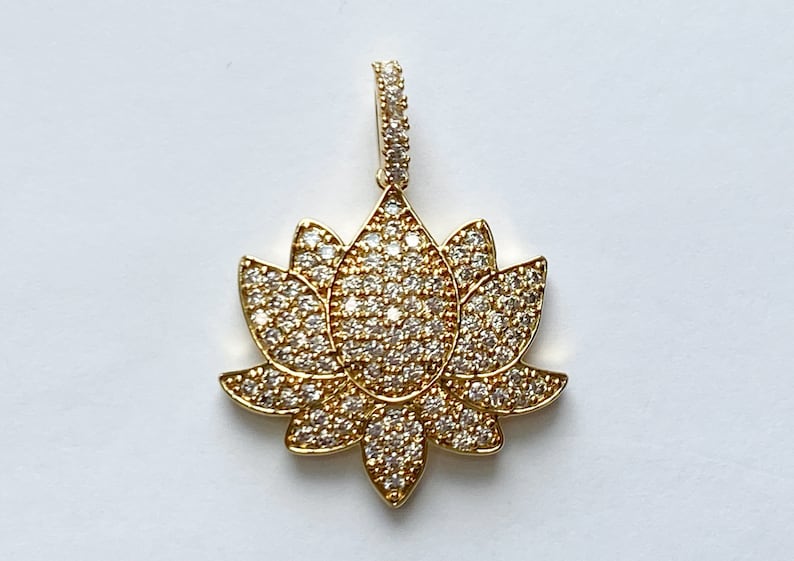 K&ouml;nnte beinhalten: Ein goldfarbener Anh&auml;nger mit einem Lotusblumen-Design, besetzt mit klaren Zirkonia-Steinen.