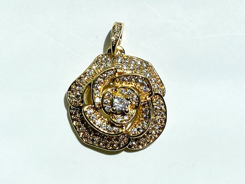 May include: A gold-tone pendant featuring a rose design with clear cubic zirconia stones.