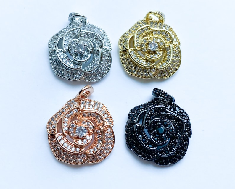 May include: Four rose-shaped pendants with clear rhinestones. The pendants are in silver, gold, rose gold, and black.