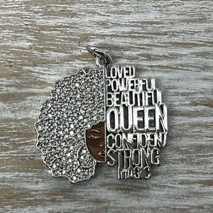 May include: Silver charm with a black woman's face and afro hair with rhinestones. The charm has the words "Loved, Powerful, Beautiful, Queen, Confident, Strong, Magic" around the face.
