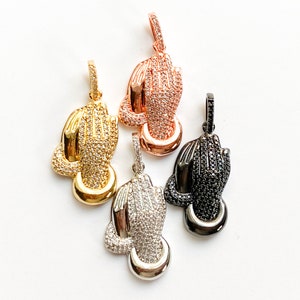 May include: Four praying hands pendants in different finishes: gold, rose gold, silver, and black. Each pendant is adorned with sparkling cubic zirconia stones.