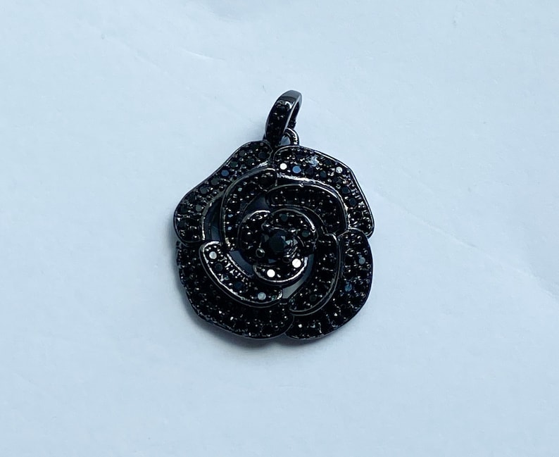May include: Black rose pendant with black crystal accents. The pendant is made of metal and has a delicate design.