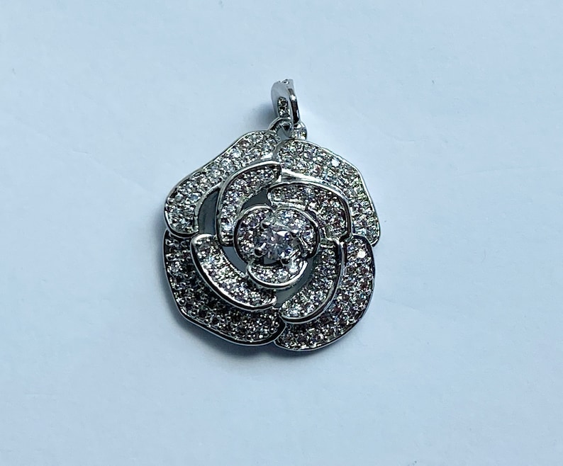 May include: Silver pendant in the shape of a rose with clear cubic zirconia stones.