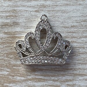 May include: A silver crown charm with clear rhinestones. The crown has a pointed top and a rounded base.