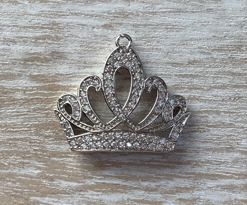 May include: A silver crown charm with clear rhinestones. The crown has a pointed top and a rounded base.