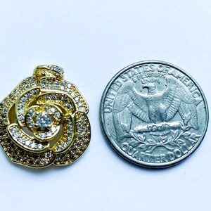 May include: A gold-tone rose pendant with clear cubic zirconia stones. The pendant is about the size of a UK 20 pence coin.