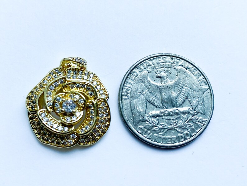 May include: A gold-tone rose pendant with clear cubic zirconia stones. The pendant is about the size of a UK 20 pence coin.
