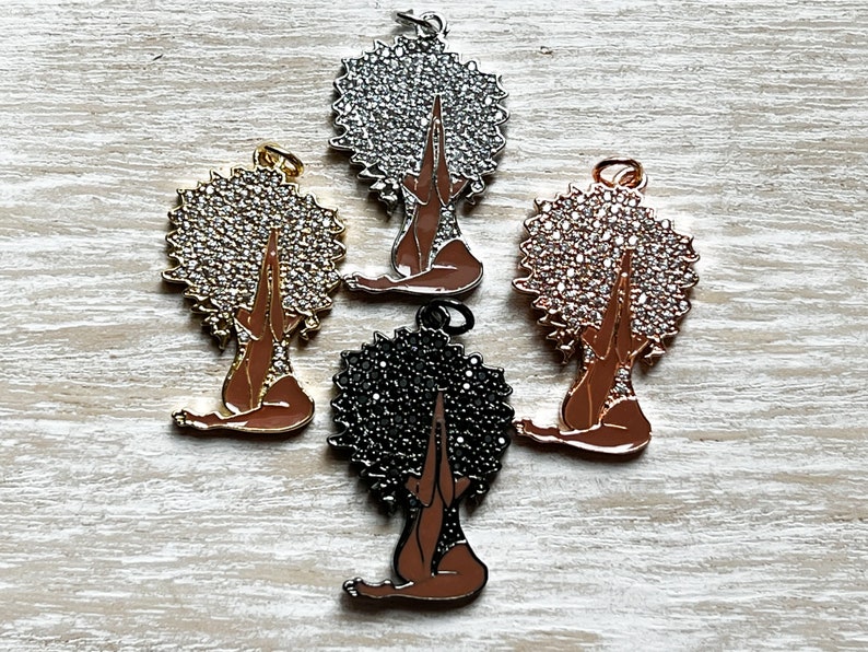 Pode incluir: Quatro pingentes que representam uma mulher com as m&atilde;os levantadas em ora&ccedil;&atilde;o. Os pingentes s&atilde;o feitos de metal e t&ecirc;m um acabamento brilhante. Os pingentes s&atilde;o de diferentes cores: prata, ouro, ouro rosa e preto.