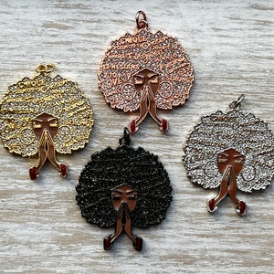 May include: Four metal charms featuring a woman with her hands clasped in prayer. The charms are in gold, silver, black, and rose gold. Each charm has a different design of words around the woman's head.