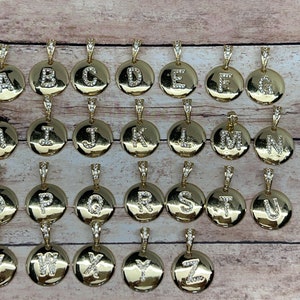 May include: A collection of gold-colored pendants, each featuring a different letter of the alphabet from A to Z. The letters are encrusted with small, clear crystals. Each pendant has a small loop at the top for a chain.