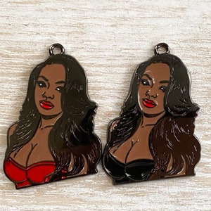 May include: Two black metal charms featuring a woman with long black hair, red lips, and a black and red outfit. The charms are in the shape of a bust and have a shiny finish.