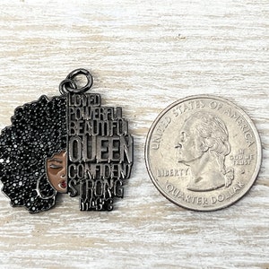 May include: Black metal charm with a silhouette of a woman with an afro and the words "Loved, Powerful, Beautiful, Queen, Confident, Strong, Magic" around her.