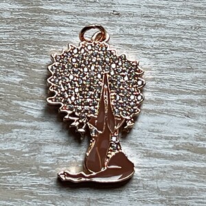 Pode incluir: Encanto dourado com uma mulher com um grande afro coberto de strass, sentada em uma postura meditativa com as m&atilde;os juntas &agrave; sua frente.