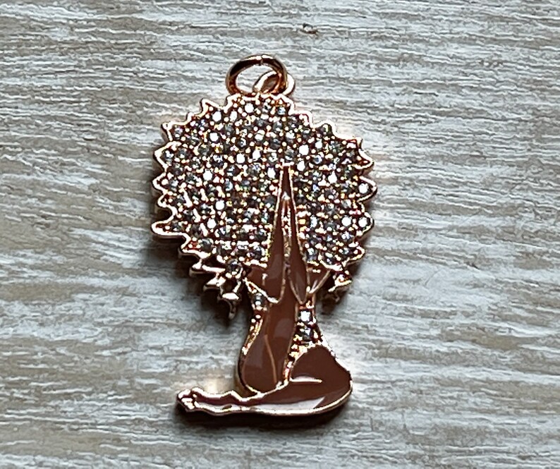 Pode incluir: Encanto dourado com uma mulher com um grande afro coberto de strass, sentada em uma postura meditativa com as m&atilde;os juntas &agrave; sua frente.
