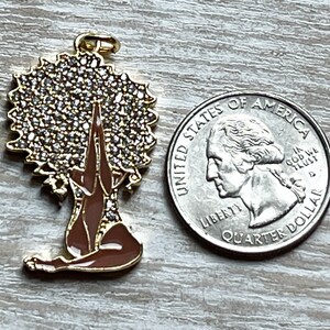 Pode incluir: Encanto de ouro com uma mulher com uma coroa de strass, sentada em uma postura meditativa com as m&atilde;os juntas em ora&ccedil;&atilde;o. O encanto &eacute; marrom e dourado.
