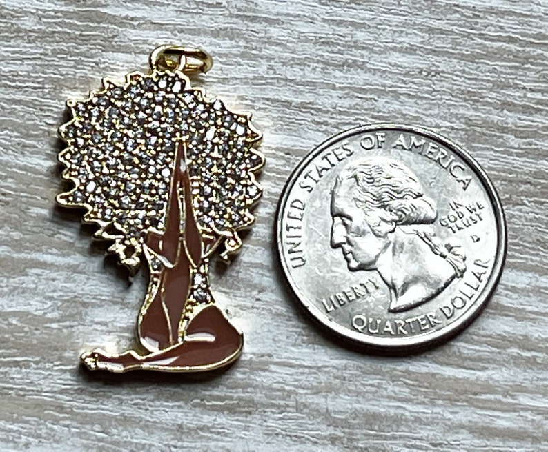 Pode incluir: Encanto de ouro com uma mulher com uma coroa de strass, sentada em uma postura meditativa com as m&atilde;os juntas em ora&ccedil;&atilde;o. O encanto &eacute; marrom e dourado.