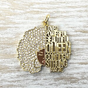 May include: Gold charm with a black woman's face and afro hair with rhinestones. The charm has the words "Loved, Powerful, Beautiful, Queen, Confident, Strong, Magic" on it.