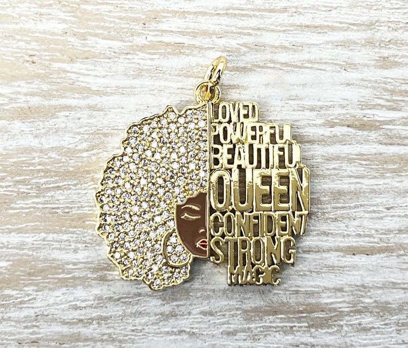 May include: Gold charm with a black woman's face and afro hair with rhinestones. The charm has the words "Loved, Powerful, Beautiful, Queen, Confident, Strong, Magic" on it.