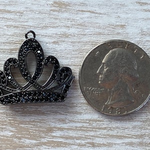 May include: A black metal crown charm with black rhinestone accents. The charm is about the size of a US quarter.