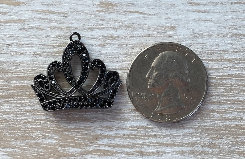 May include: A black metal crown charm with black rhinestone accents. The charm is about the size of a US quarter.