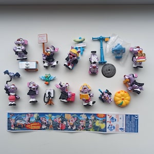 Puede incluir: Una colección de pequeñas figuras de ratones morados con varios accesorios, incluyendo un murciélago, una cámara y una calabaza. Algunos ratones visten capas y sostienen letreros. Un envoltorio de caramelos de colores está en la parte inferior.