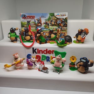 Pode incluir: Uma coleção de figuras de brinquedos Kinder Surpresa com toupeiras de desenhos animados e outros personagens. Os brinquedos estão em várias poses e cenários, com cores vibrantes e designs detalhados. Um logotipo colorido da Kinder Surpresa é visível.