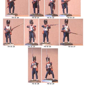 May include: Nine miniature figures of French soldiers from the Imperial Guard, wearing blue and red uniforms with white accents, holding muskets and standing on a brown surface. The figures are labelled with numbers from 20 to 29.