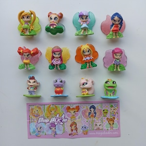 Op de afbeelding: Een verzameling van twaalf kleine plastic Pop Pixie-figuurtjes met diverse personages met kleurrijke vleugels en voetjes, vergezeld door een rechthoekig papieren inzetstuk met illustraties en de tekst Pop Pixie en magickinder.com.