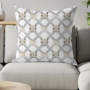 May include: A square throw pillow featuring a white background with a repeating lattice pattern composed of intersecting gray and beige textured lines, creating a diamond grid design with small geometric accents at each intersection point.