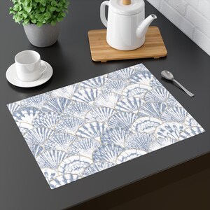 May include: A blue and white placemat with a pattern of seashells. The placemat is on a dark gray surface.