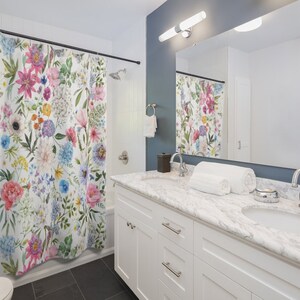 May include: A white bathroom with a floral shower curtain, a white vanity with two sinks, and a large mirror above the sinks.